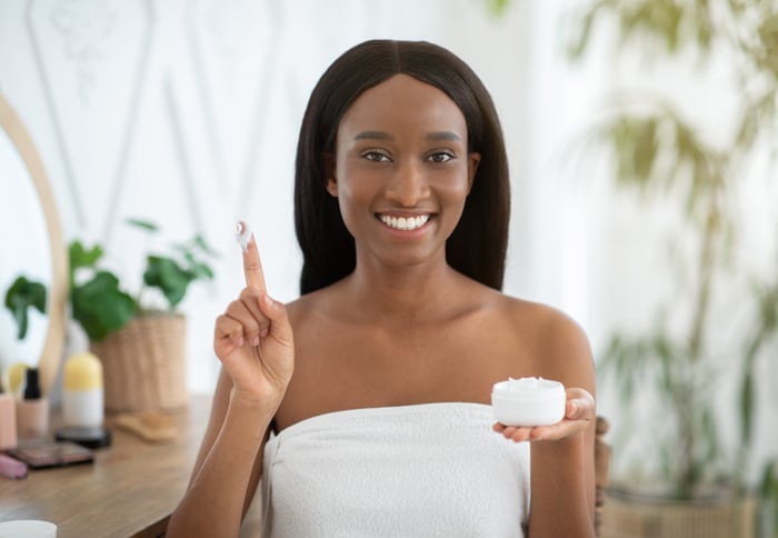 A person holding a bottle of skin creme with a finger up in the air.