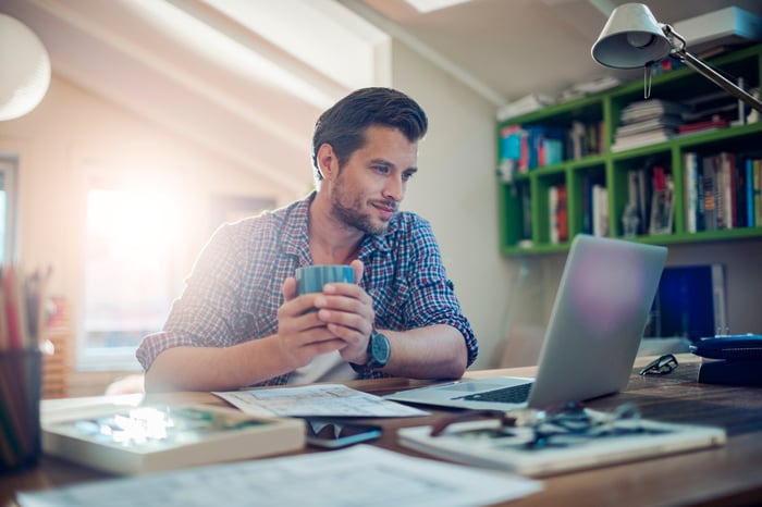 A person at a laptop holding a mug.