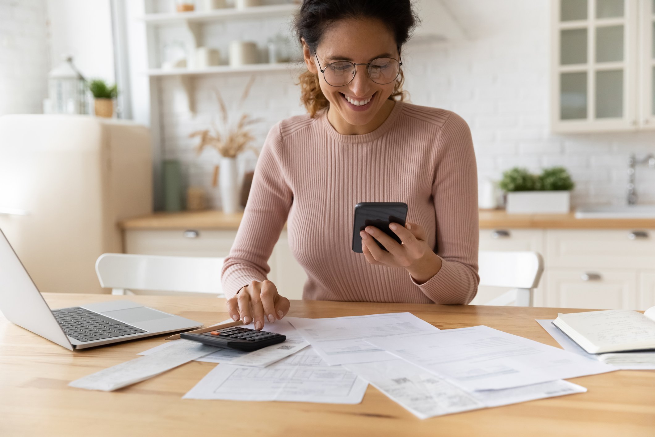 Smiling person looking at smartphone and typing on calculator