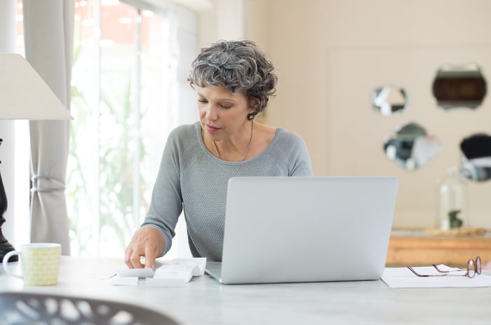 A person looking at a document while sitting in front of a laptop.