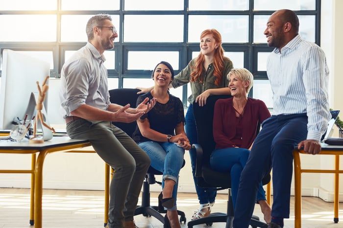 A team of five employees laughing while talking in the office.