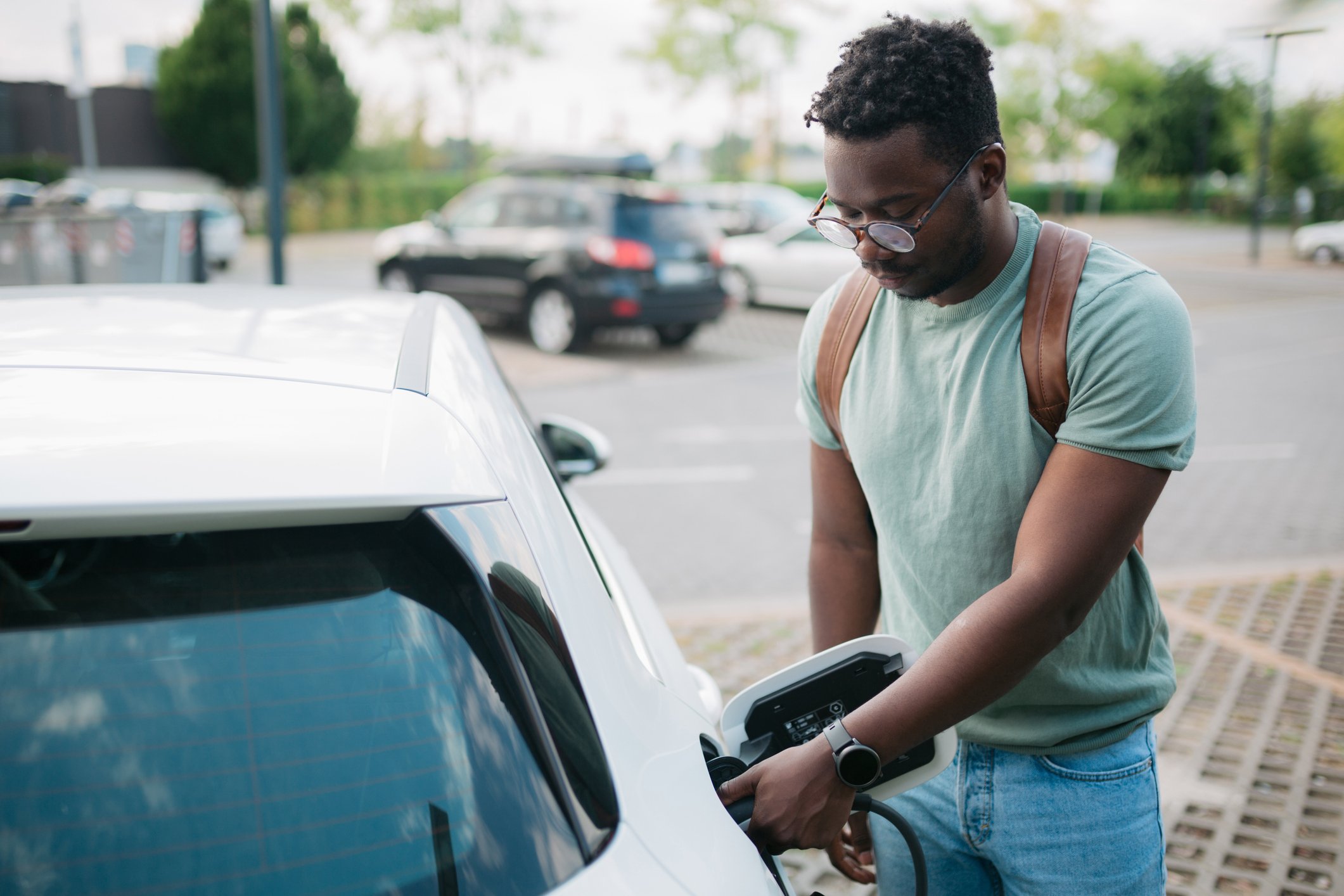 a driver charges an electric vehicle at a charging station.