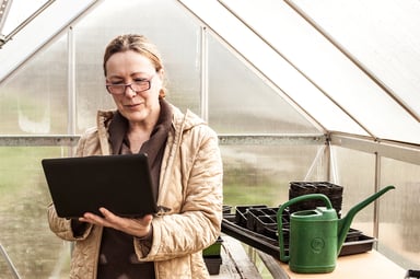 mature woman with glasses and laptop in greenhouse