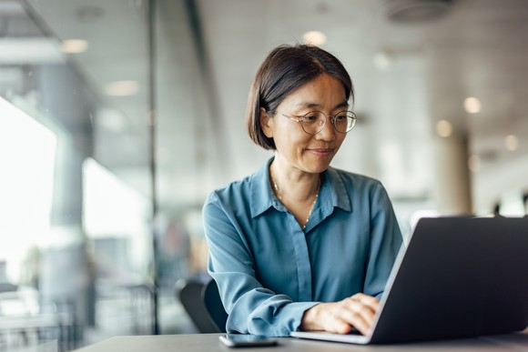 Seated person smiling at an open laptop.