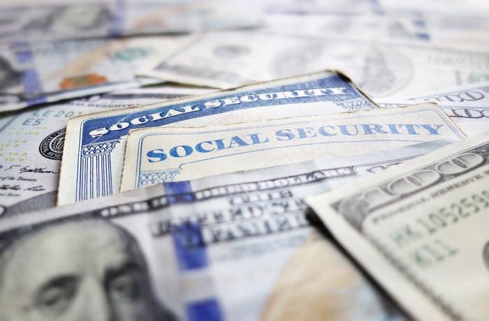 Two Social Security cards set atop a messy pile of one hundred dollar bills.