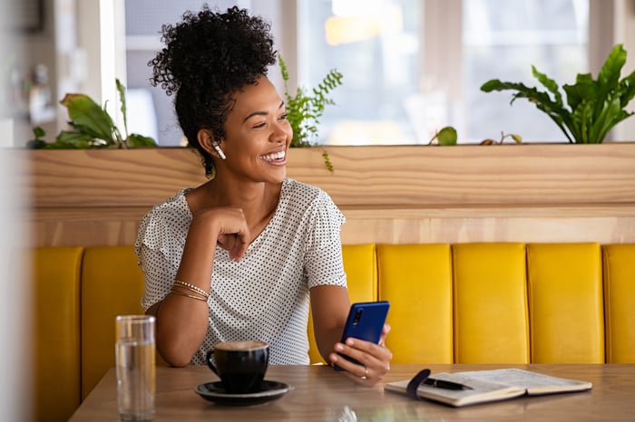 Smiling person holding a phone while sitting in a restaurant booth.