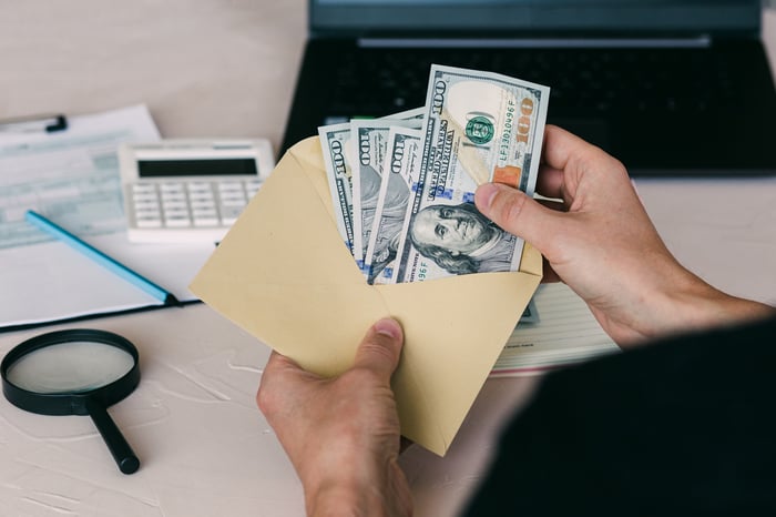 A person opening an envelope full of $100 bills.