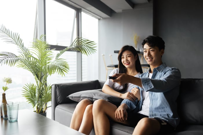 Two people sitting on a couch while one points a remote forward.