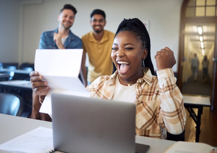 A smart person sitting in a classroom looking at a document and pumping their fist in victory.