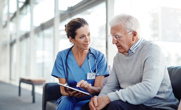 A person wearing scrubs talking to a seated person.