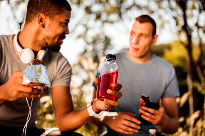 Two friends eating energy bars and drinking energy drinks after a workout.