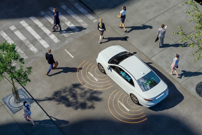 A digital render of a self-driving car stopped at a cross walk surrounded by people.