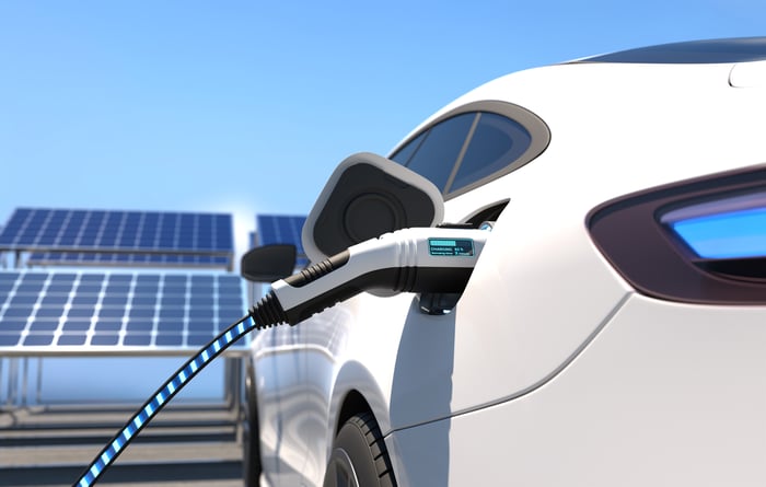 An electric vehicle plugged in for charging while parked in front of solar panels.