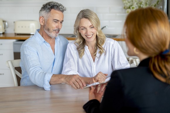Two people across from someone showing them a tablet.