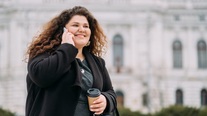 Smiling person outdoors, talking on phone.