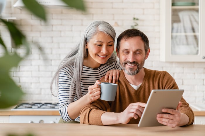 Two people standing in a kitchen looking at a tablet.