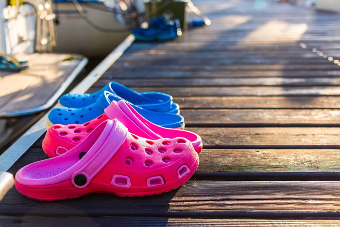 Two pairs of brightly colored plastic clogs on a beach boardwalk.