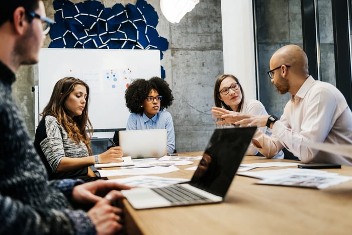 A group of five colleagues seated at a large table and collaborating at work.