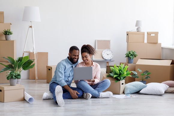 Two people surrounded by moving boxes, using a laptop computer.