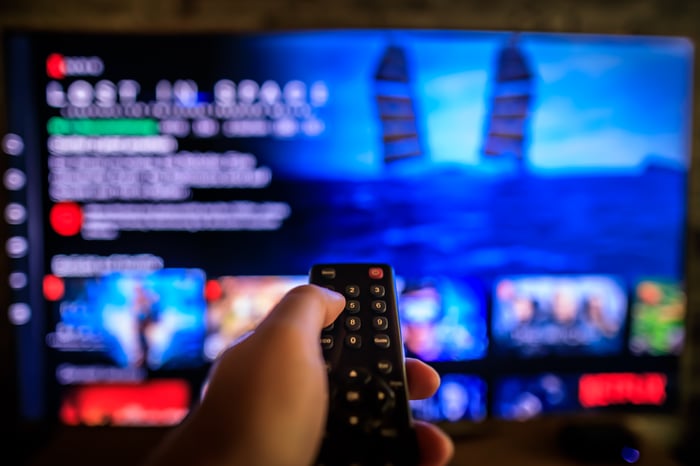 Hand pointing remote at TV showing streaming service.