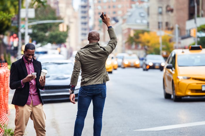 One person trying to hail a taxi, while their friend orders an Uber on their smartphone.