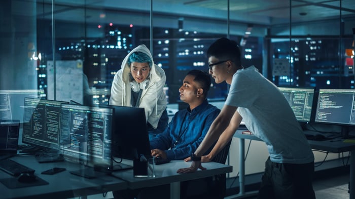 A team of IT professionals looking at a computer inside a dark office.