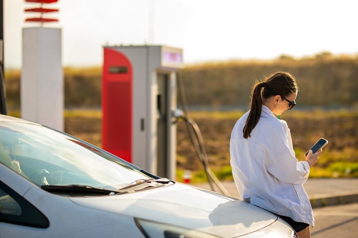 A person looks at their phone while charging an electric vehicle.