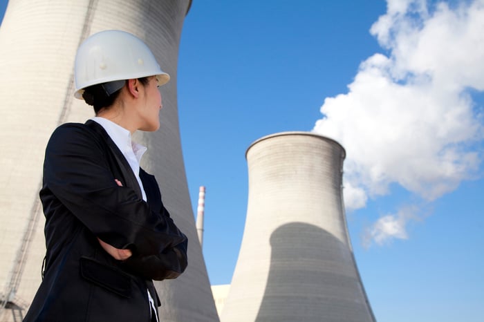 A person in a hard hat and suit standing in front of a nuclear power plant.