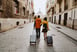 two people walk a paved city street towing luggage