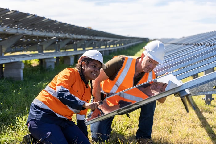 Two people wearing personal protective equipment work on a solar farm.