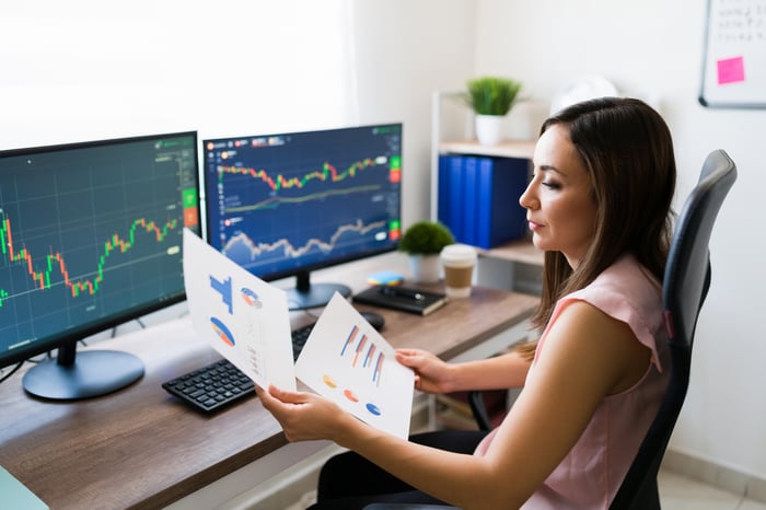 Person reviewing charts and graphs on a computer and printouts.