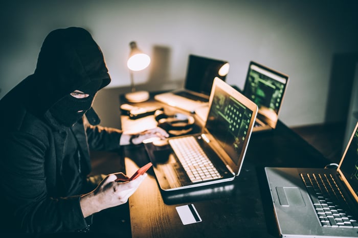 A computer hacker wearning a mask while working on four different laptop computers.