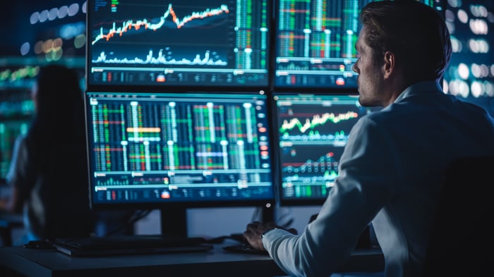 A closeup of a person reviewing graphs across multiple large computer monitors.