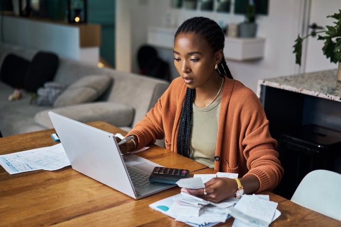 An image of a person at a desk reviewing paperwork and working on a laptop.