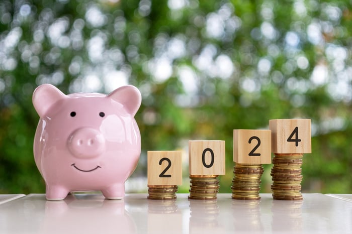 A piggy bank next to piles of coins in ascending order supporting blocks spelling 2024.