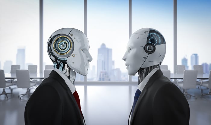 Two androids in business suits meet in a high-rise office.