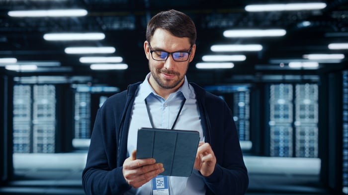 A person looking down at a tablet device while standing in a data center.