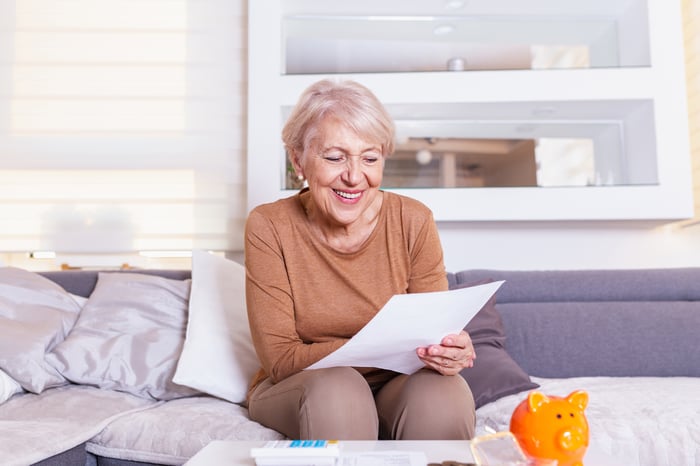 A smiling person seated and holding a document.