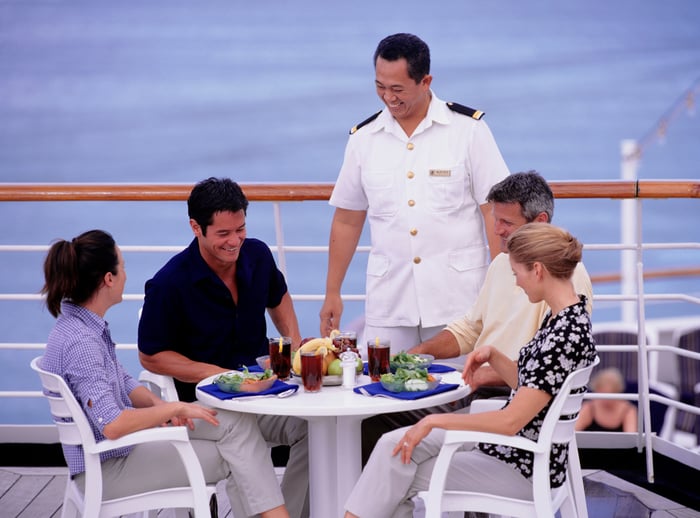 Two couples eating on a cruise ship with a staff member talking to them.