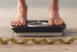 Man stands on a weight scale with a flexible ruler in the foreground.
