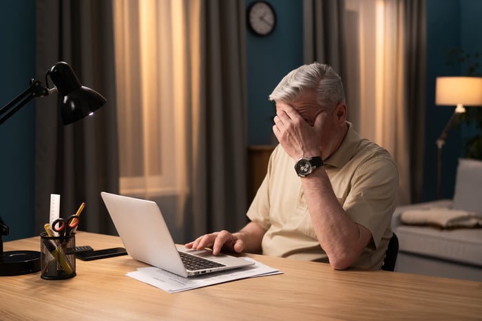 A person at a laptop covering their face.