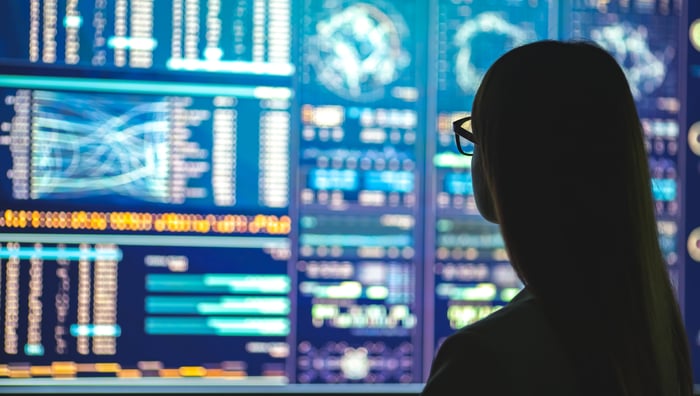 A businessperson silhouetted against a backdrop of monitors displaying various graphs.