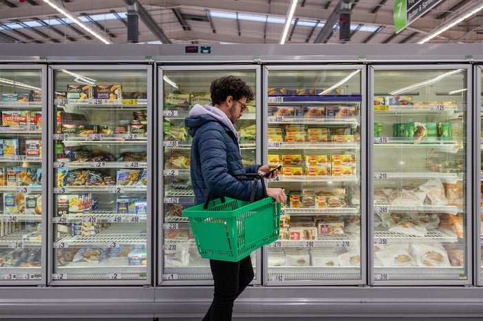 A person walking in the frozen food isle of a grocery store looking at their phone.