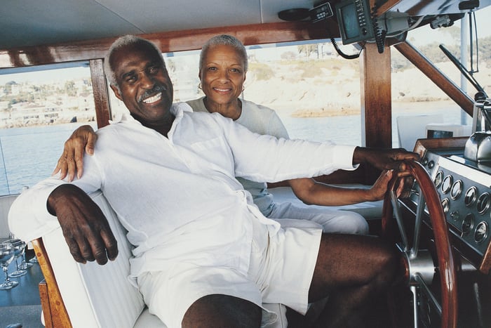 Two people sitting beside each other on a boat with a hand each on the steering wheel.