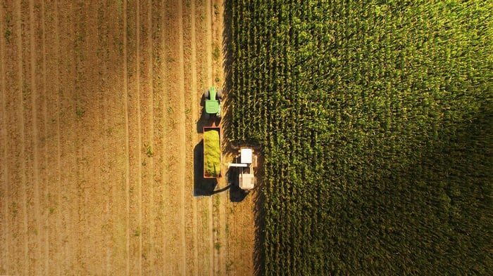 Harvester and loading truck working in a cornfield viewed from above.