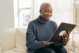 older person sitting on a couch looking at a tablet