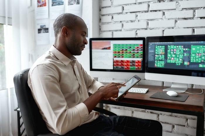 A person sitting at a desk with computer monitors and a tablet.