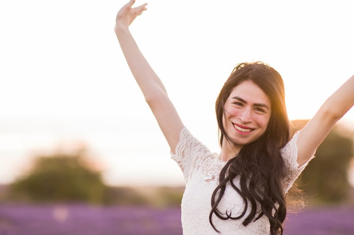 A person smiling outdoors, with arms outstretched. 