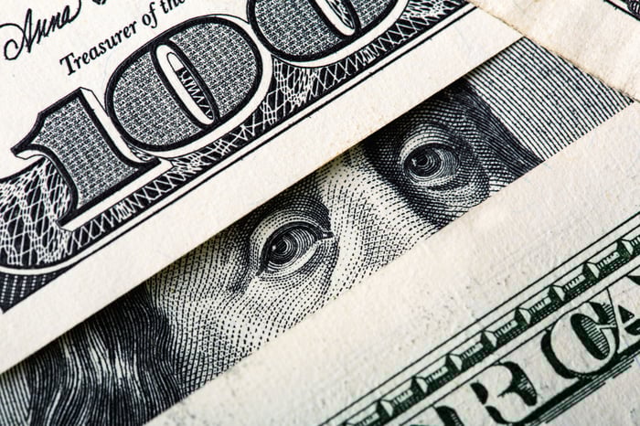 Ben Franklin's eyes peering between a messy pile of one hundred dollar bills.