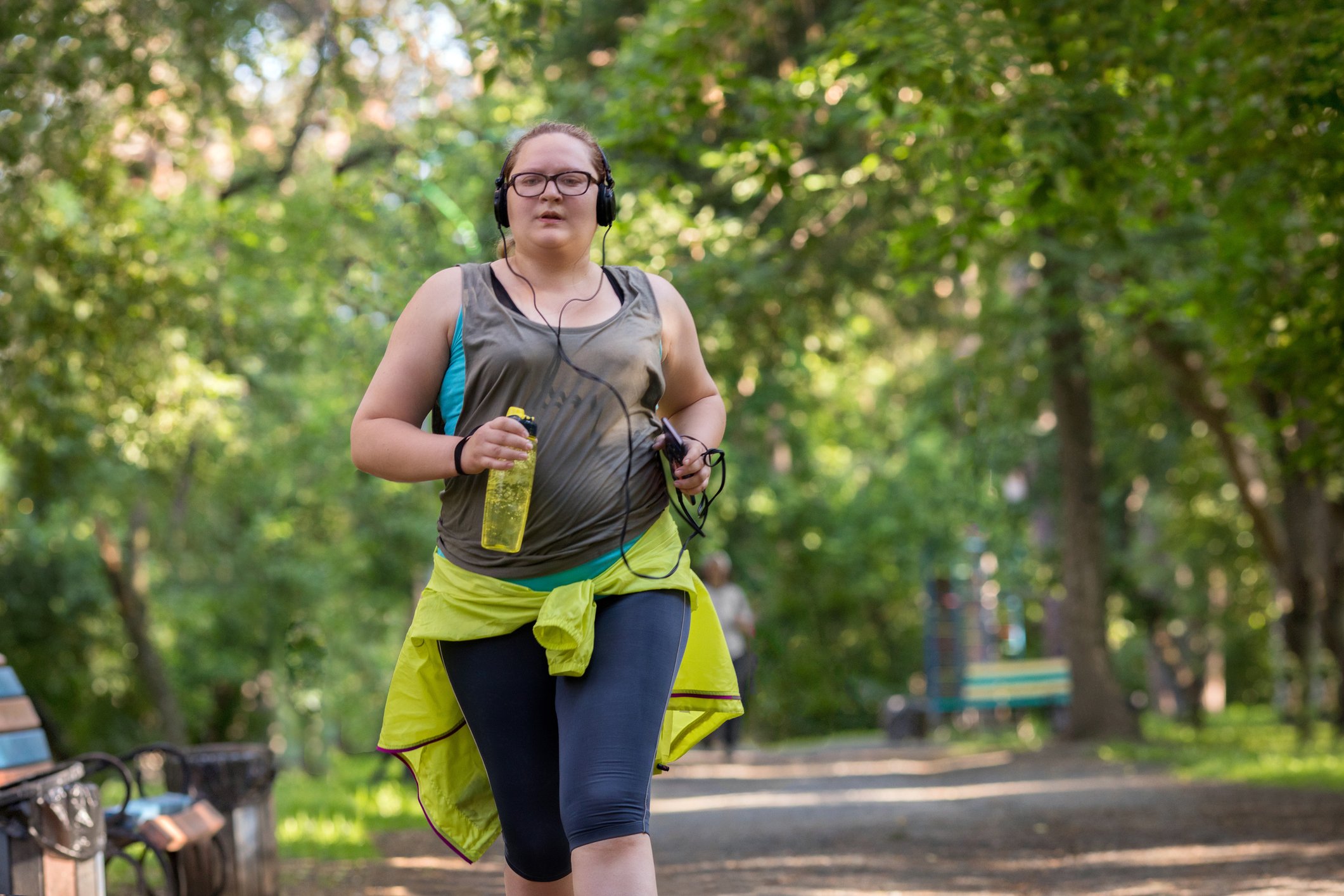 woman running in the park with a bottle of water listening to music